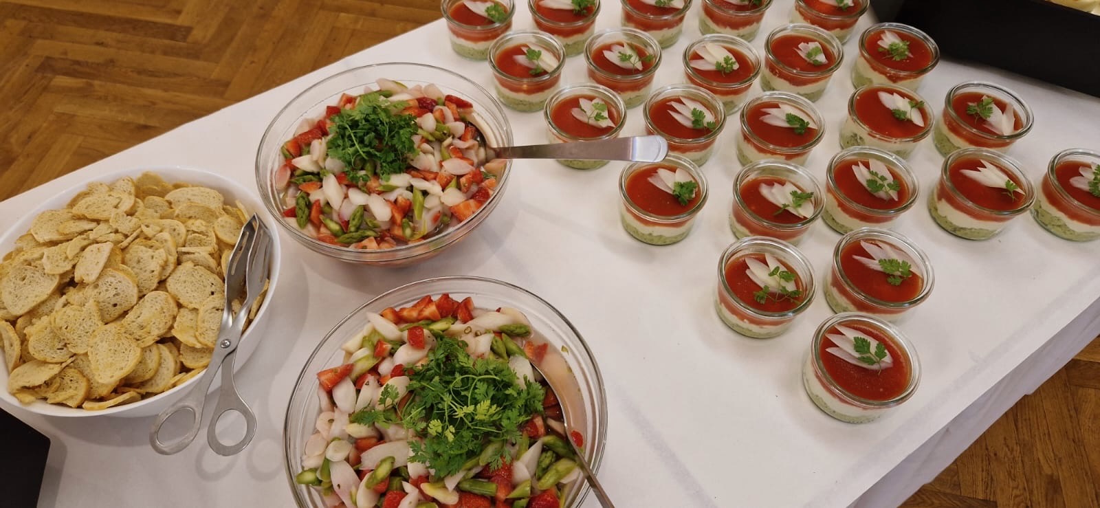 Buffetvorschlag: Auf einem Tisch mit Stofftischdecke sind zwei Salatschüsseln mit einem bunten Spargel-Erdbeersalat, ein Brotkorb und zahlreiche kleine Weckgläser mit Vorspeisen angerichtet.