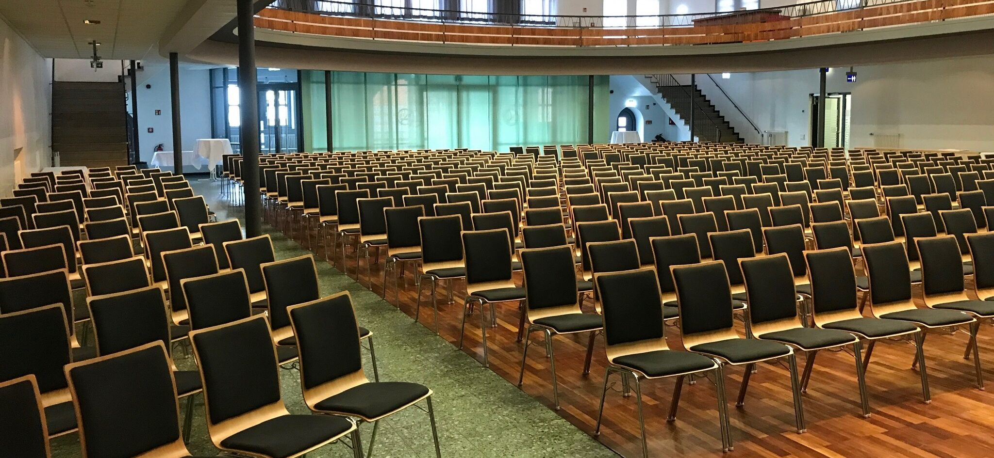 Stadthalle Groß-Gerau in Parlamentarischer Bestuhlung: großer Saal mit Empore. Das Parkett ist bestuhlt mit von mehreren Gängen geteilten Stuhlreihen. Sitzplätze für mehrere hundert Menschen.