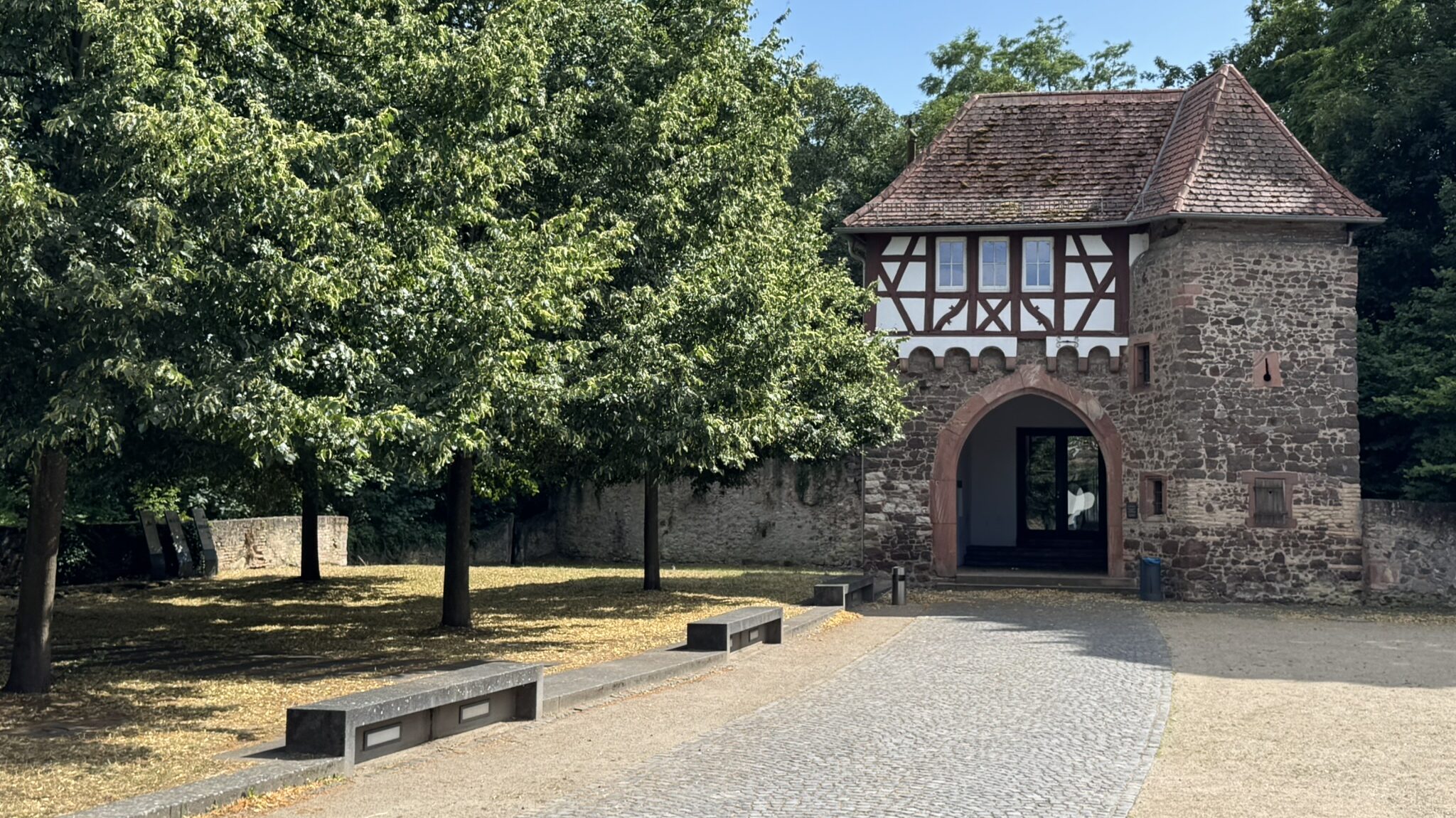 Schloß Dornberg: Historisches Torgebäude mit alten Steinmaunern und Fachwerk. Davor ein Hof mit Pflastersteinen, Bänken und Bäumen.