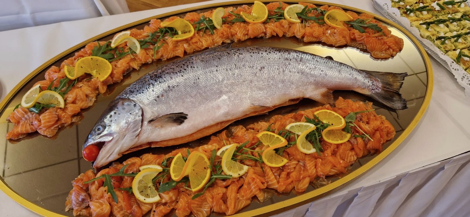 Buffet-Vorschlag: Auf einem großen Spiegelteller sind Filtes vom Räucherlachs in einem Oval angerichtet. In der Mitte liegt ein ganzer Lachs mit einer Cocktailtomate im Maul.
